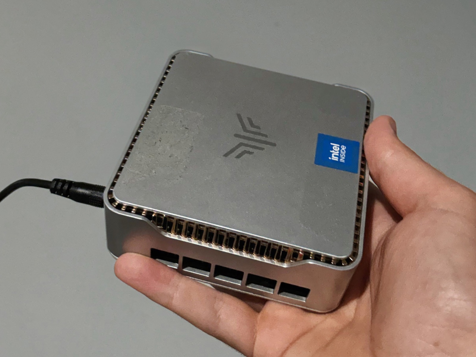 A silver mini PC, plugged in and running as an Uncloud Storage Node, held in one hand